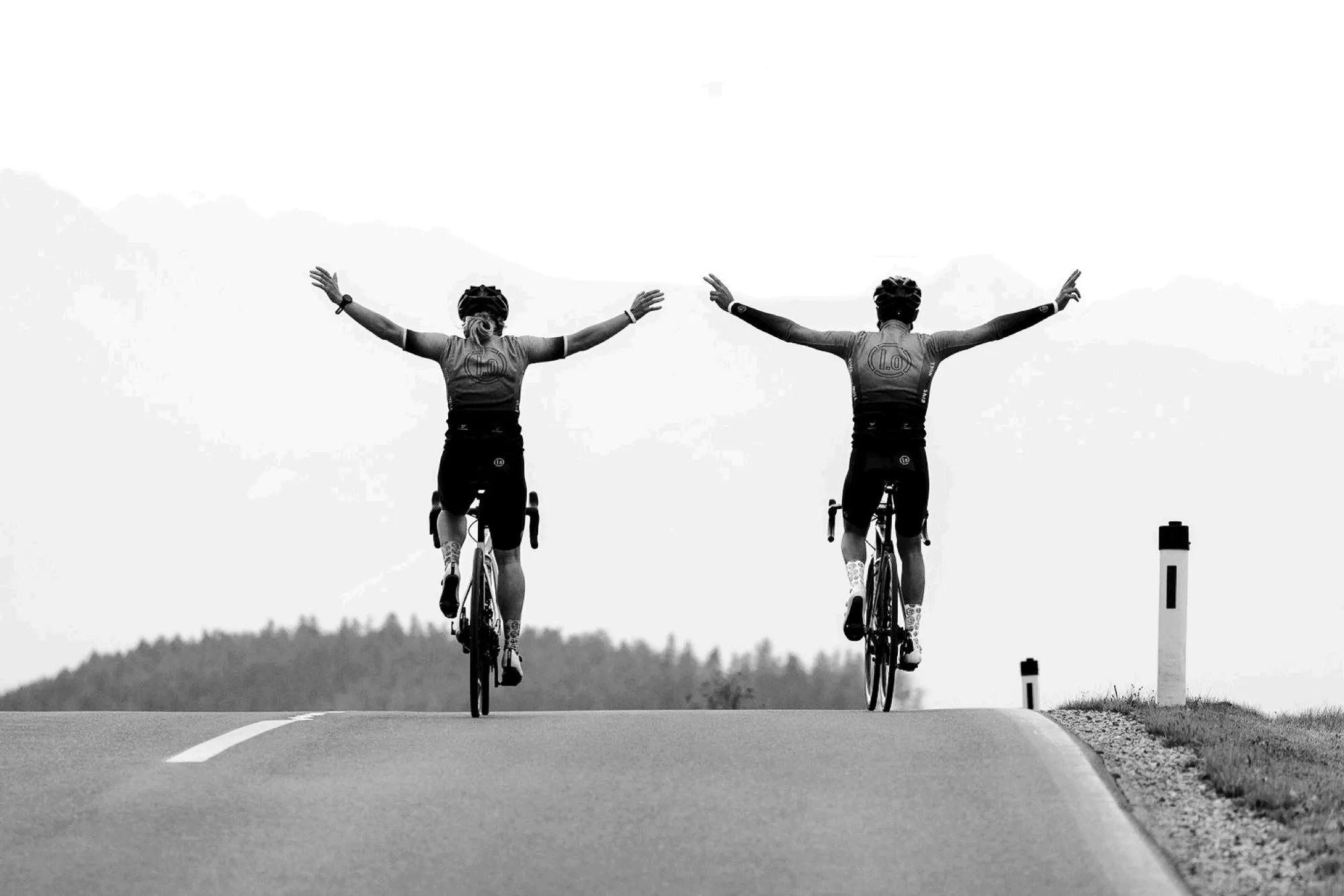 Zwei Radsportler mit ausgebreiteten Armen auf einer Landstraße