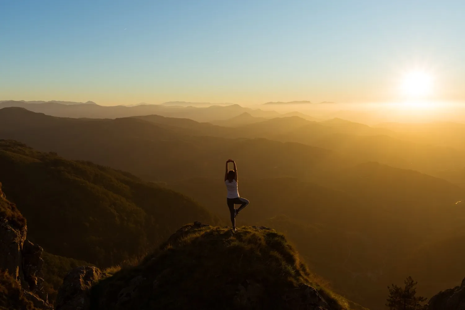 Frau in Yoga-Pose auf einem Berggipfel bei Sonnenuntergang